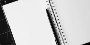 Top view of an open spiral notebook with a black pen on a cutting mat, perfect for creative projects.