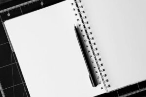 Top view of an open spiral notebook with a black pen on a cutting mat, perfect for creative projects.