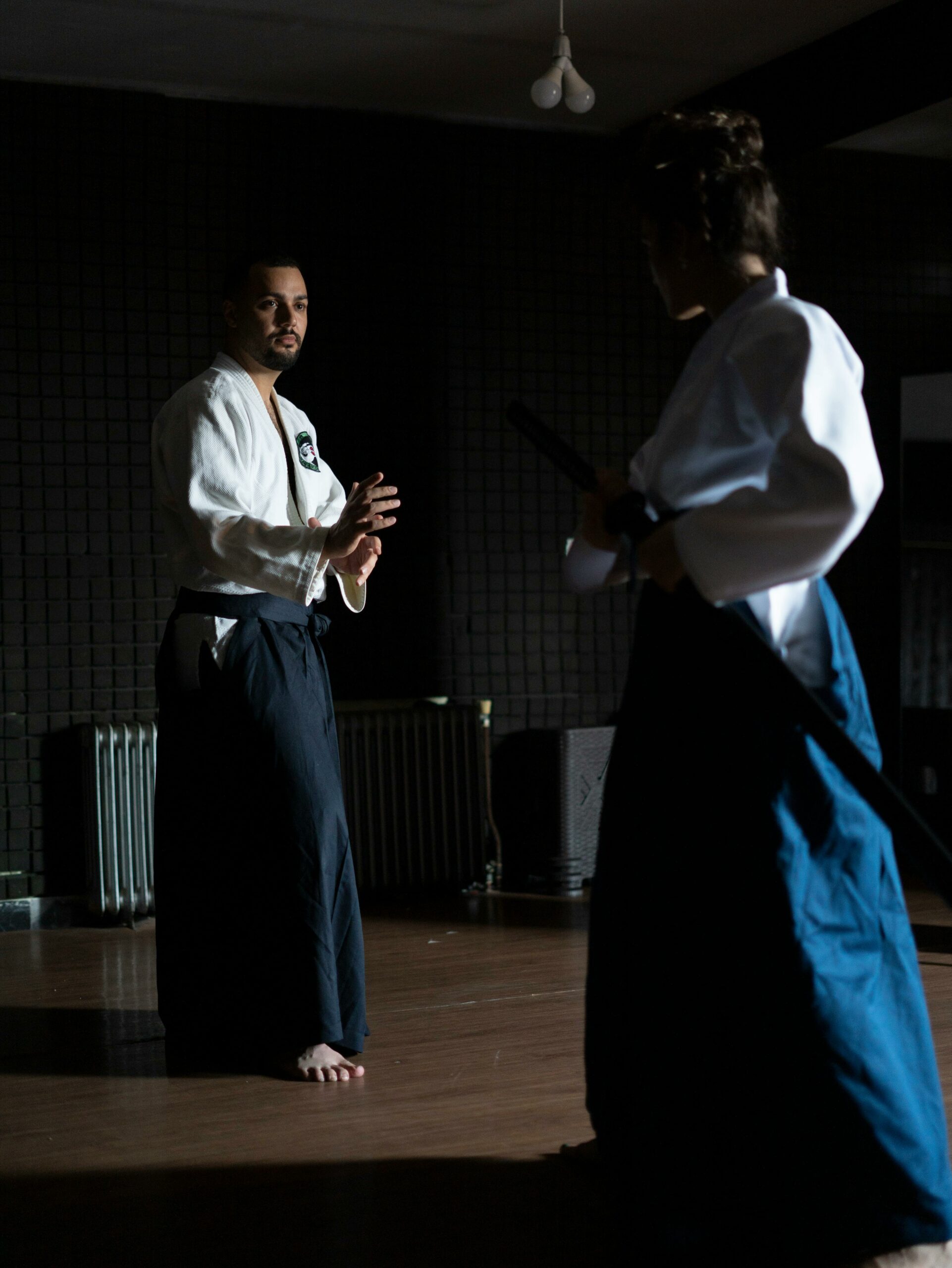 Two adults practicing martial arts in a dimly lit dojo, focused and poised.