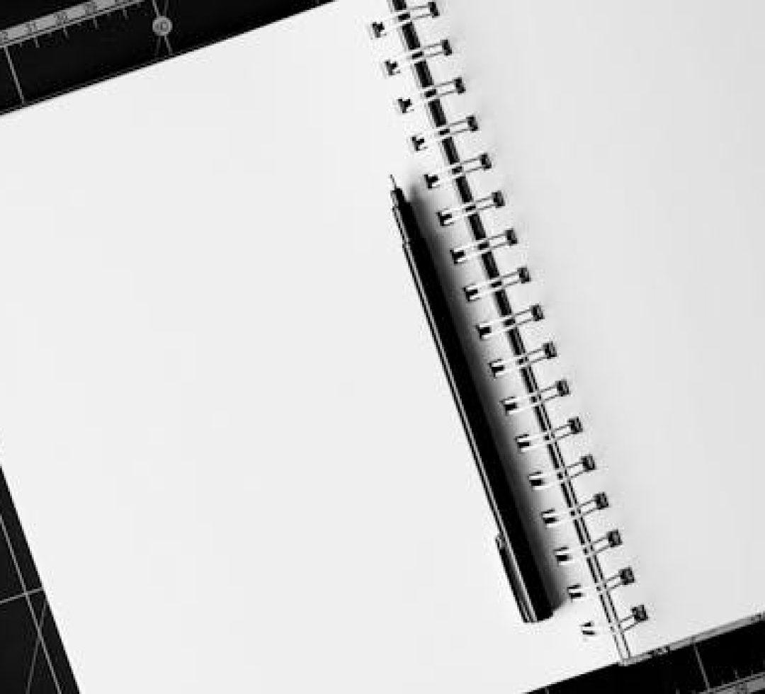Top view of an open spiral notebook with a black pen on a cutting mat, perfect for creative projects.
