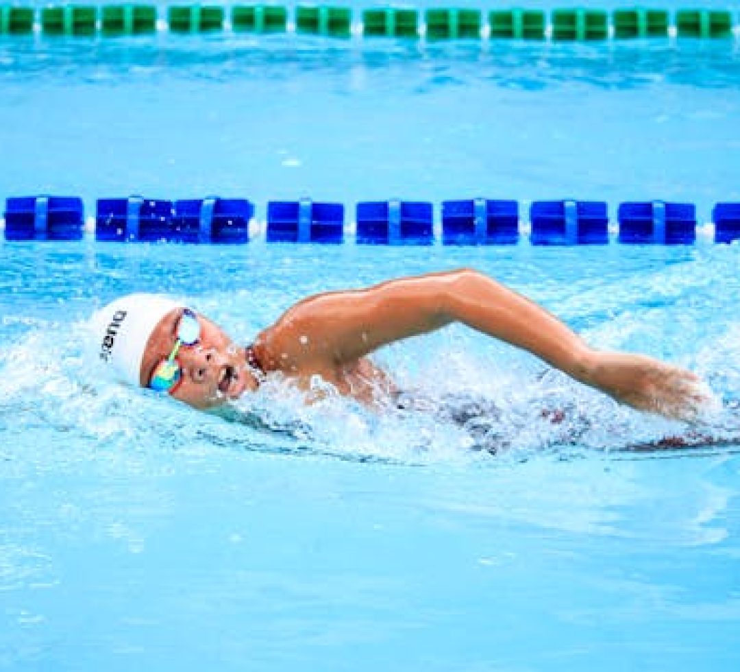 A swimmer energetically performs a freestyle stroke in a clear outdoor swimming pool, showcasing competitive spirit.