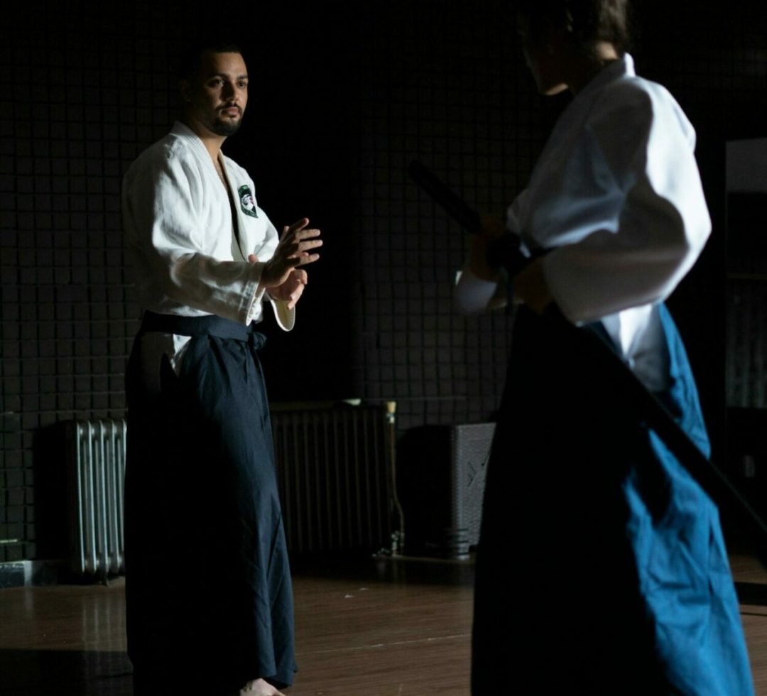 Two adults practicing martial arts in a dimly lit dojo, focused and poised.