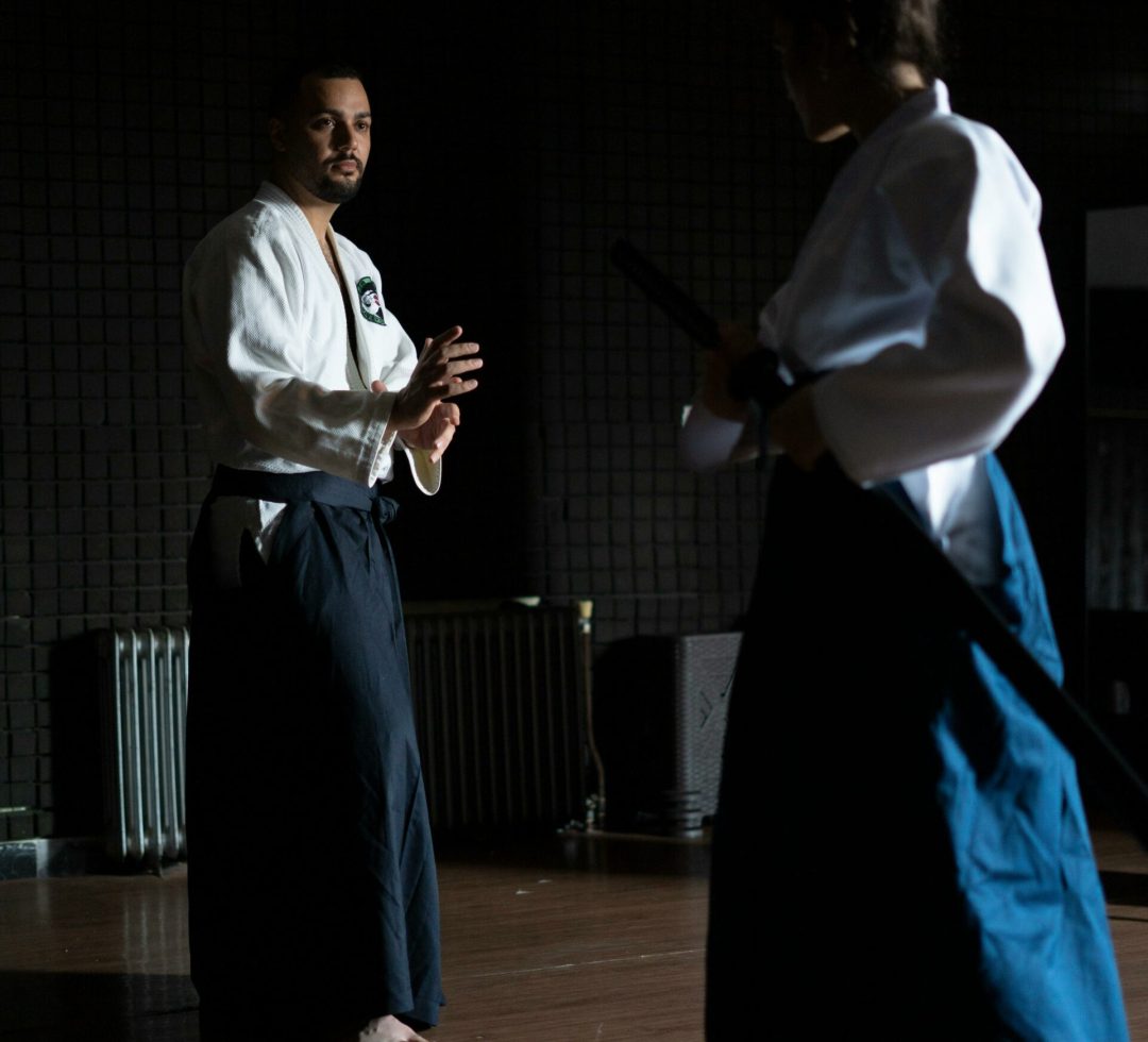 Two adults practicing martial arts in a dimly lit dojo, focused and poised.